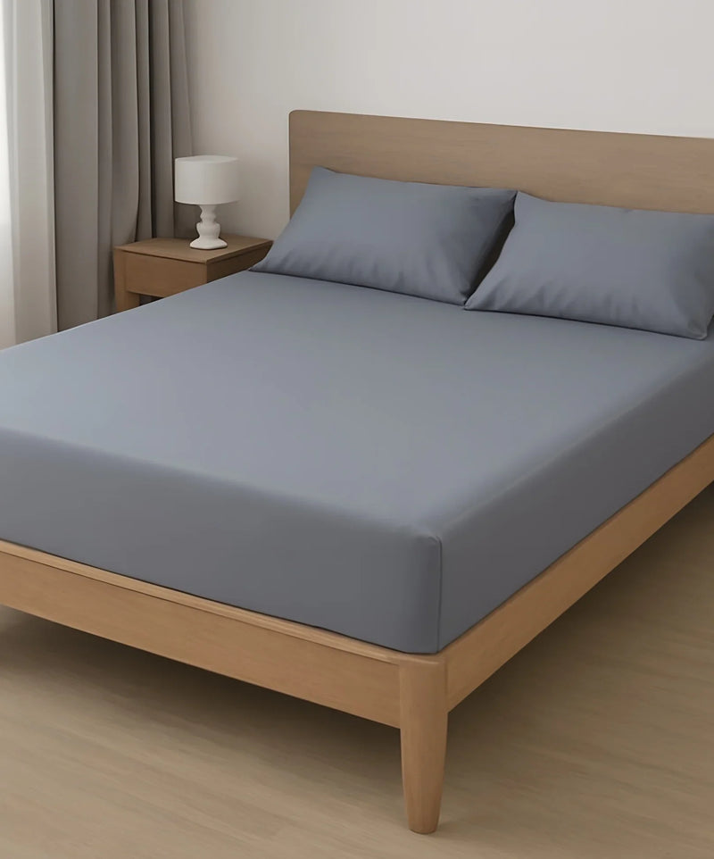 Minimalist bedroom with wood bed frame, gray fitted sheet, two pillows, and nightstand